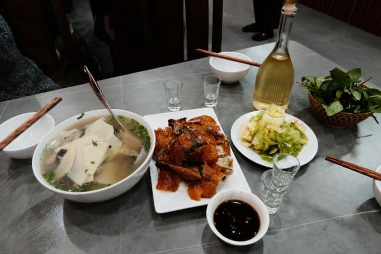 Jantar composto por sopa com fatias de cogumelo, pato assado crocante, legumes refogados, molho e ervas frescas em mesa moderna