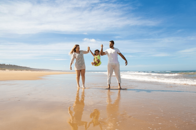 Casal sorrindo enquanto levanta sua filha na praia em um dia ensolarado, simbolizando a alegria de morar no litoral