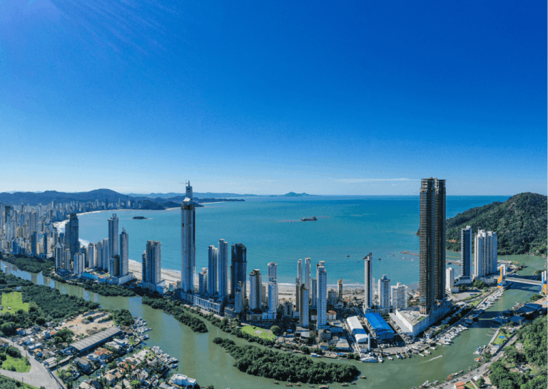 Panorâmica aérea de Balneário Camboriú com arranha-céus ao longo da orla curva e mar azul-turquesa ao fundo