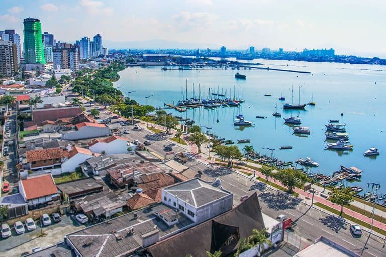 Vista aérea da Beira Rio no bairro Fazenda em Itajaí, com barcos atracados e edifícios residenciais ao fundo.